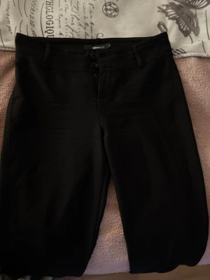 Svarta kostymbyxor bootcut-byxor från Gina Tricot - Snygga svarta bootcut-byxor från Gina Tricot. Byxorna har en klassisk siluett med utsvängda ben och är tillverkade i ett mjukt, slätt material som ger en stilren look. Perfekta för dig som gillar trendiga och bekväma byxor.