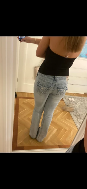 True Religion ljusblå bootcut jeans - Säljer ett par ljusblå jeans från True Religion med bootcut passform och låg midja. Jeansen har snygga broderade detaljer på bakfickorna och klassisk femficksdesign. Materialet är jeans