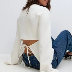 Vit långärmad topp med öppen rygg - Snygg vit långärmad topp med croppad passform och öppen rygg som knyts med band. Perfekt för dig som vill ha en stilren men ändå unik look. Tunn och mjuk känsla i materialet, passar till både jeans och kjol.