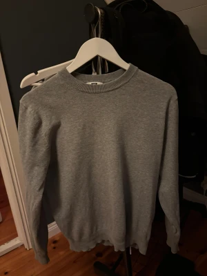 Grå långärmad tröja i bomull - En enkel och stilren grå långärmad tröja med rund hals. Tröjan är tillverkad i mjuk bomull och har ribbade muddar vid hals, ärmslut och nederkant. Perfekt för dig som gillar en clean och chill look.