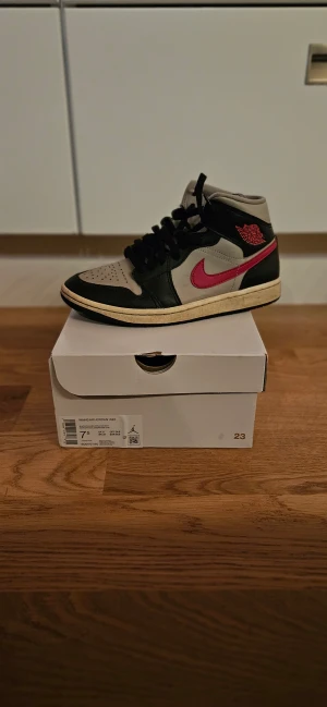 Nike Air Jordan 1 Mid College Grey - Nike Air Jordan 1 Mid i college grey, svart och gym röd. Snygg high-top sneaker med klassisk Jordan-logga och röd swoosh på sidan. Skon har snörning, rund tå och platt sula. Materialet är skinn och syntet, vilket ger en premiumkänsla och bra komfort. Kan sänka priset vid snabba affärer