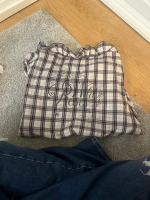 Rutig kortärmad blus Hilfiger Denim - Supersöt rutig blus från Hilfiger Denim i vitt, blått och lila. Den har volangkrage, korta puffärmar med resår och knappar framtill. Lätt och luftig bomull, perfekt för en chill och trendig look.