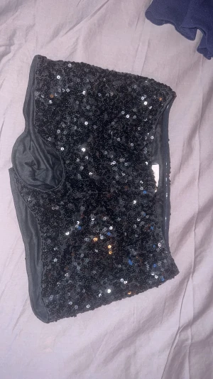Svart paljett shorts ifrån Nelly - Säljer ett par svarta glitter shorts från Nelly i storlek 34, täckt med glittriga paljetter som ger en riktigt snygg och festlig vibe perfekta till nyår.