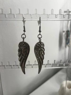 Silvriga örhängen med vingar - Säljer ett par coola silvriga örhängen formade som detaljerade änglavingar. Hängande modell med snygg struktur som ger dem en unik look. Perfekt för dig som gillar statement-smycken och vill sticka ut.💕💕