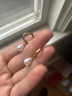 Guldplaterad  18 k örhängen - Säljer ett par snygga örhängen i stål guldplaterad 18 k med droppformade vita pärlor. De har en enkel ringdesign och pärlan hänger elegant nedanför. Perfekta för dig som gillar stilrena smycken med en touch av klass. Titta gärna min profil, finns i Gbg 