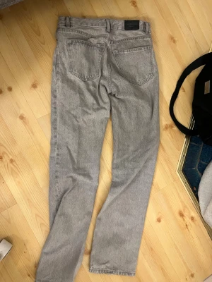 Gråa jeans - Säljer ett par grå jeans med klassisk straight fit. Jeansen har normal midja, knappgylf och är tillverkade i slitstarkt bomullsjeansmaterial. Perfekt för dig som gillar tidlös stil och vill ha ett par jeans som funkar till allt.