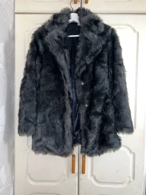 Mörkgrå pälsjacka med krage - Säljer en fluffig och snygg mörkgrå pälsjacka med bred krage och knäppning framtill. Jackan har lång ärm och är perfekt för dig som vill ha en statement piece till vintern. Fodrad insida för extra komfort och värme. (Inga defekter eller liknande)