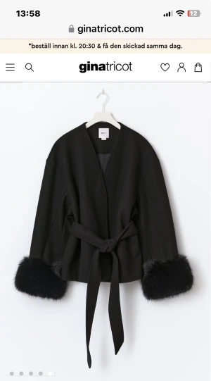 Svart kappa med pälsdetaljer Gina Tricot - Svart kappa från Gina Tricot med fluffiga pälsdetaljer vid ärmsluten och knytband i midjan. Jackan har en loose passform, omlottstil och lång ärm. Perfekt för dig som vill ha en stilren look med extra edge.