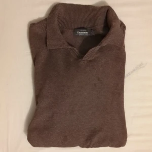 Brun pikétröja Dressmann Supima M - Brun pikétröja från Dressmann i mjuk Supima bomull. Klassisk krage och v-ringad hals, ribbade muddar vid ärmslut och nederkant. Långärmad och med normal passform, perfekt för dig som gillar stilren och enkel look.