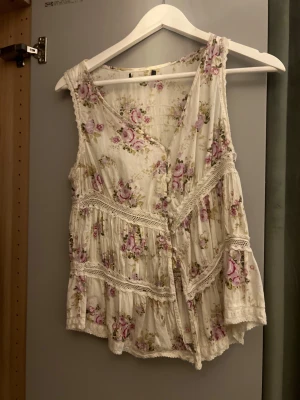 Blommig ärmlös linnetopp med spets - Romantisk ärmlös linnetopp i ljusbeige med rosa och lila blommor. 