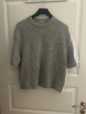 Grå stickad tröja  - Snygg grå stickad tröja från gina med korta ärmar och rund hals. Perfekt för dig som gillar enkel och stilren design. Mjuk och skön känsla tack vare det stickade materialet. Passar till jeans eller kjol för en chill look.