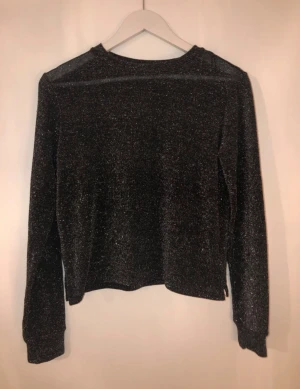 Glittrig svart långärmad topp H&M Divided - Säljer en svart långärmad topp från H&M Divided i storlek XS. Toppen har ett glittrigt tyg som ger en snygg shimmer-effekt.