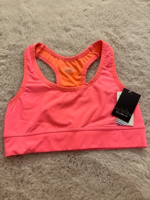 Rosa sporttopp från C/fit  - Sport-topp från C/fit i storlek XS. Den är i helt nytt skick med prislappen kvar!!!😇 Den har en racerback-design med orange meshpartier på ryggen för extra ventilation!!. Tillverkad i mjukt och stretchigt syntetmaterial som passar perfekt till träning. 