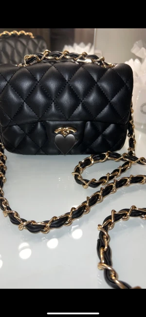 Svart quiltad axelväska med kedja - Säljer en svart quiltad axelväska som har en klassisk guld och svart kedja. Väskan har en elegant CC detalj framtill. Har använt väskan endast en gång. För fler bilder hör gärna av dig 💕