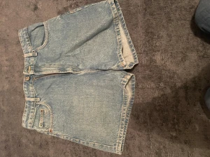Ljusblå jeansshorts från Zara - Säljer ett par klassiska ljusblå jeansshorts från Zara i storlek 38. De har normal passform, fem fickor och bälteshällor. Perfekta för varma dagar med sin tidlösa denimlook och raka ben. Stängs med knapp och dragkedja framtill.