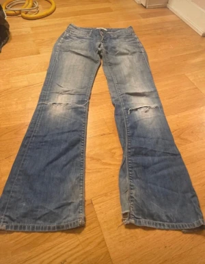Levis 572 bootcut jeans blå - Snygga Levis 572 bootcut jeans i ljusblå tvätt med slitningar och hål på knäna. Klassisk femficksmodell med låg midja och bootcut-ben. Jeansen har en avslappnad vibe och är tillverkade i mjukt denimtyg. midja 35 innerbenslängden 75
