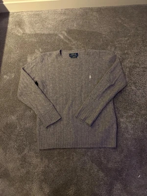 Grå kabelstickad tröja Polo Ralph Lauren - Säljer denna snygga kabel stickade Ralph lauren tröjan i 90% ull och 10%kashmir. Passar dig runt 165. Priset är en hugget i sten och diskuteras gärna.