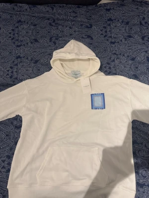 Vit hoodie från Casablanca med blått tryck - Säljer en fräsch vit hoodie från Casablanca med stor blå grafisk ruta och texten 'CASA BLANCA' på ryggen och mindre tryck på bröstet. Hoodien har huva, känguruficka och långa ärmar. Perfekt för dig som gillar stilrena streetwear-plagg.