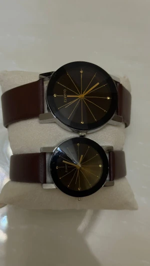 Svart och brun duo-klocka Quartz - Säljer ett set med två stilrena klockor från Quartz. Båda har svart urtavla med guldiga linjer och detaljer, samt brunt läderband. Klockorna har rund form och silverfärgat hölje. Perfekt för dig som gillar minimalistisk design och matchande accessoarer.