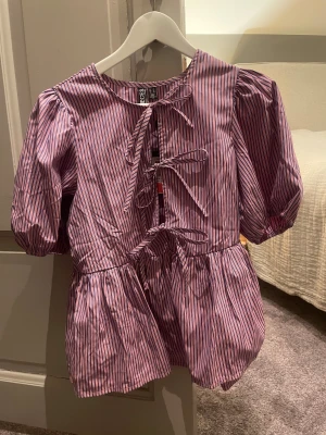 Randig topp från Pieces - Superfin topp från Pieces i rosa och blått med smala ränder😻 Toppen har puffiga korta ärmar och flera snörningar framtill. Jag säljer den pga att den inte kommit till använding❣️