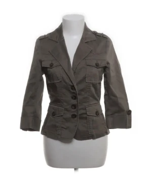 Grå kavaj från Stockh LM, storlek 36 - Snygg grå kavaj från Stockh LM med klassisk krage, trekvartsärmar och fyra framfickor med lock och knapp. Jackan har markerad midja och knäpps med fem knappar framtill. Perfekt för dig som gillar stilrena och coola detaljer.