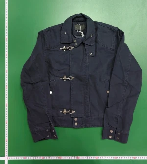 Mörkblå parkajacka med metallspännen - Parkajacka i mörkblå bomull med coola metallspännen framtill och hög krage. Jackan har långa ärmar, knappar vid mudden och två sidofickor med knappstängning. Snygg, rak passform som ger en chill vibe och funkar till många olika stilar.