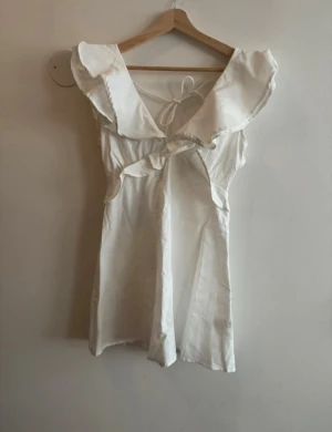 Vit klänning med volang från Boohoo - Supersöt klänning från Boohoo med breda volangdetaljer vid axlarna och omlott framtill. 