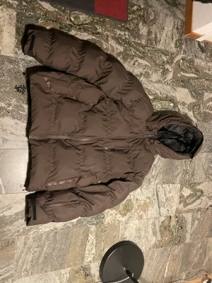 Brun pufferjacka från Jack & Jones - Säljer en brun pufferjacka från Jack & Jones Core med huva och dragkedja framtill. Jackan har två sidofickor med dragkedja och justerbara muddar vid ärmslut. Perfekt för kalla dagar och har en schysst, lite loose passform. I