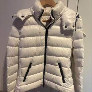 Vit Moncler pufferjacka med dragkedja - Säljer en snygg vit pufferjacka från Moncler.   Köptes för flera år sedan och har inte använts på några vintrar, jag har dessutom kemtvättat jackan så är nästintill helt ren utan några fläckar.  Storleken i jackan säger (1) vilket motsvarar ungefär S/Xs, passar mig bra som oftast har Xs  Kvittot för jackan finns och ingår vid köp! 