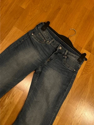 Blå bootcut jeans med hög midja - Snygga blå jeans med bootcut passform och hög midja. Klassisk femficksmodell med dragkedja och knapp framtill. Jeansen har en lätt tvättad look och är tillverkade i jeansmaterial med skön stretch. Perfekta för dig som gillar retrovibbar och bekväm stil.