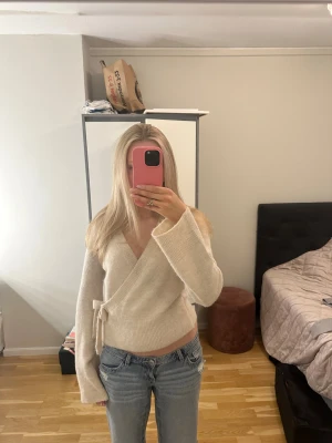 Kräm vit stickad omlott tröja från Gina Tricot st 170 - Säljer en super fin omlott tröja i stickat material från Gina Tricot. Tröjan har långa ärmar och en söt rosett i sidan. Den är endast använd ett fåtal gånger och är i mycket bra skick!🎀