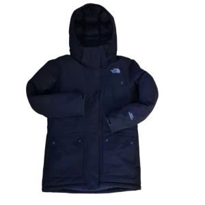 Svart dunparkas från The North Face - Säljer en svart dunparkas från The North Face med huva, stora fickor och diskret logga på bröstet. Jackan har lång ärm, dragkedja och knappar framtill. Insidan är fodrad med värmande material och jackan är perfekt för kalla vinterdagar.