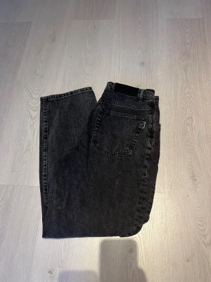 Svarta jeans från WOODBIRD wide fit - Säljer ett par svarta jeans från WOODBIRD med bred passform och raka ben. Jeansen har klassisk femficksdesign, bälteshällor och en svart WOODBIRD-label bak i midjan. Materialet är robust denim och färgen är tvättad svart för en cool look.