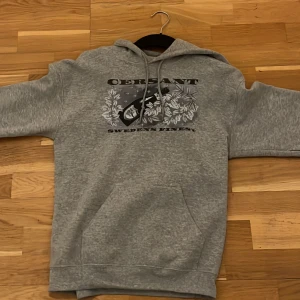 Grå hoodie från Cersant med tryck - (Limited edition så den säljs ej mer på deras sida) Säljer en grå hoodie från Cersant med stort tryck på bröstet som visar en flaska och blommor. Tröjan har huva med snörning, magficka och långa ärmar. Perfekt för dig som gillar streetwear och vill ha en chill look.