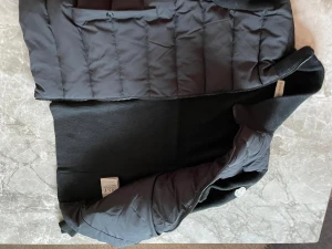 Svart Cardigan från Moncler - Svart dunväst från Moncler med quiltad front och stickade sidor. Västen har en dragkedja och detaljer i marinblått med röda ränder samt Moncler-logga på bröstet. Snyggt sportig look med ribbad struktur och tydlig Moncler-text längs axeln.