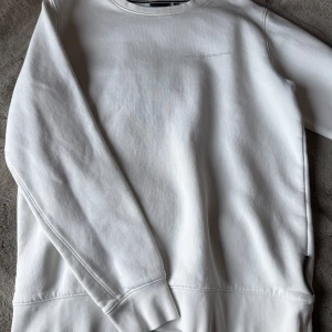 Vit sweatshirt från Sail Racing M - Vit sweatshirt från Sail Racing i storlek M. Tröjan har en stilren design med diskret logga på bröstet och mjuk insida. Rund hals och ribbade muddar vid ärmslut och nederkant. Perfekt för chill dagar och enkel att matcha med jeans.
