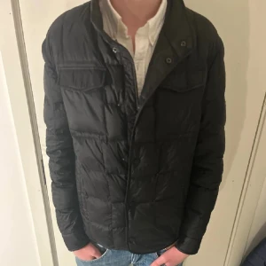 Massimo dutti jacka - Svart massimo dutti jacka med quiltad design och knappar framtill. Jackan har två bröstfickor med lock och långärmad passform. Perfekt för dig som vill ha en stilren och enkel look under kyliga dagar.