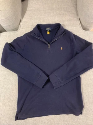 Marinblå half zip tröja Polo Ralph Lauren - Snygg marinblå långärmad tröja från Polo Ralph Lauren i storlek S. Klassisk design med half zip och liten broderad logga på bröstet. Mjuk bomullskvalitet och normal passform, perfekt för chill dagar. Enkelt att matcha med jeans eller joggers.