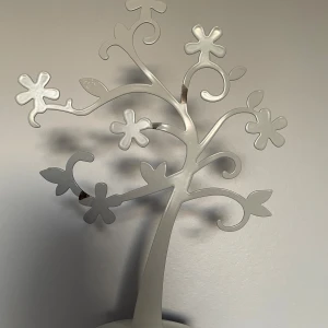 Vitt blommigt smyckesträd - Snyggt smyckesträd i vitfärgad metall med blommiga detaljer och böjda grenar. Perfekt för att hänga ringar, armband, halsband och örhängen. en cool inredningsdetalj för ditt rum. Går att böja enkelt. 