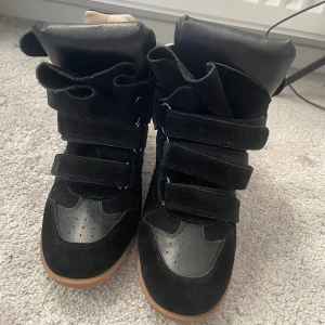 Isabel Marant svarta - Säljer ett par svarta wedge sneakers från Isabel Marant med cool design och kardborreband. Skorna har en blandning av mocka och skinn, beige insida och brun gummisula. 