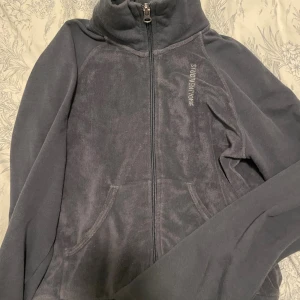 Mörkgrå/blå fleece hoodie från Nike - Säljer en mörkgrå hoodie från Nike i mjuk fleece med dragkedja hela vägen och hög krage. Tröjan har fickor framtill och diskret Nike-logga på bröstet. Perfekt för chill dagar eller när du vill vara extra bekväm.