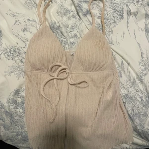 Beige linnetopp från Amisu med knyt - Supersöt beige linnetopp från Amisu med smala axelband och snygg knytning framtill. Toppen har en lätt rynkad struktur och v-ringad form som ger en trendig look. Perfekt för varma dagar och enkel att styla med jeans eller kjol.