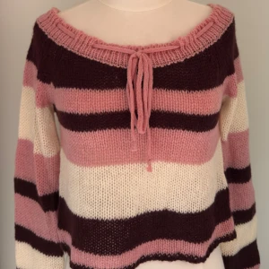 Randig stickad tröja med snörning - Supermysig stickad tröja med breda ränder i rosa, vinrött och vitt. Tröjan har en snygg snörning vid den breda halsringningen och långa ärmar. Perfekt för dig som gillar en chill och färgglad stil.