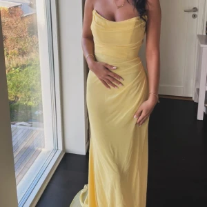 Ljusgul axelbandslös långklänning, finns även band att lägga på som kommer med i köpet! - Superfin ljusgul långklänning med axelbandslös (finns även axelband att lägga på) design och draperad överdel. Klänningen har en figurnära passform och faller snyggt längs kroppen. Perfekt för dig som vill sticka ut med en elegant och stilren look. Köpt för 3000kr även insydd lite extra i midjan för att ge extra figur till kroppen. Använd endast en kväll! Kommer på en galje i klänningens egen påse! 