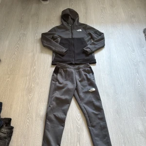 Grå mjukisbyxor från The North Face - Säljer ett par grå mjukisbyxor från The North Face med svart detalj vid fickorna och vit logga på benet. Byxorna har elastisk midja och är tillverkade i mjukt material, perfekta för chill eller träning.