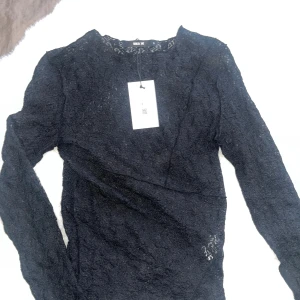 Svart spetsblus från Bik Bok - Säljer en svart långärmad blus från Bik Bok i storlek S. Blusen är helgjord i tunn spets med snyggt mönster och har en rund halsringning. Toppen är oanvänd, endast testad med lappen kvar. Slut i butik. Nypris 299kr