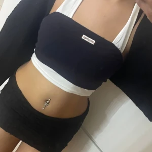 Svart och vit crop top med breda band - Säljer en snygg croppad topp  med breda axelband. Toppen är svart med vita detaljer och har en tydlig logga framtill. Den har raka linjer och är figurnära, perfekt för dig som gillar en sportig och trendig look.