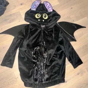 Svart fladdermus-hoodie halloween kostym  - Supergullig svart hoodie med fladdermusvingar, stora gula ögon och glittriga lila öron på huvan. Tröjan är i mjuk sammet och har dragkedja framtill. Perfekt för halloween eller maskerad!🦇 👻  både för flickor och pojkar 🧑‍🧑‍🧒‍🧒