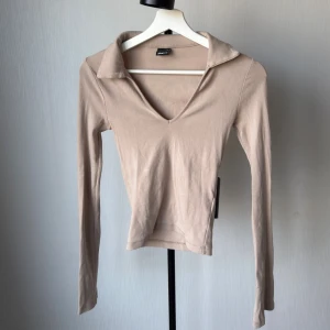 Beige långärmad topp från Gina Tricot - Säljer en stilren beige långärmad topp från Gina Tricot i mjuk bomull. Toppen har klassisk krage och är figurnära med enkel design, perfekt att matcha med jeans eller kjol. Supersnygg att ha som basplagg och passar dig som gillar neutrala färger.