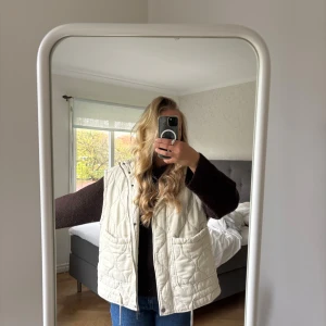  vit dunväst med dragkedja - Säljer en vit dunväst med stora fickor framtill och dragkedja samt tryckknappar. Västen har en avslappnad passform och är perfekt att slänga över en hoodie eller stickad tröja. Snyggt mönster i tyget och riktigt skön att bära under höst och vinter.